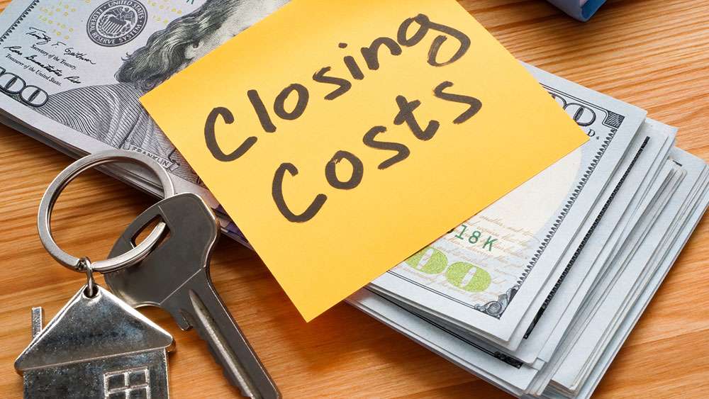 Stack of money with the words "Closing Costs" next to a house key.